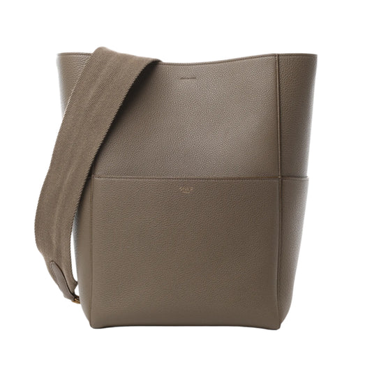 Front view of CELINE Seau Sangle Bucket Leather Shoulder Bag in greige grained leather with wide matching fabric shoulder strap and clean, structured lines, displayed against a white background.