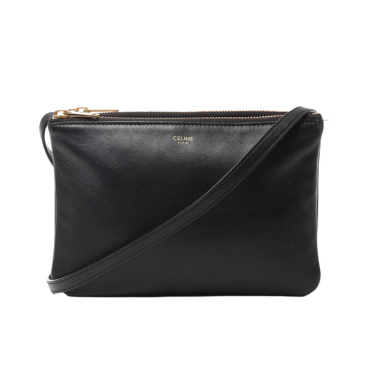 Front view of Celine Trio Small Leather Crossbody Bag in black with gold-tone zippers, three compartments, and adjustable leather strap, displayed against a white background.