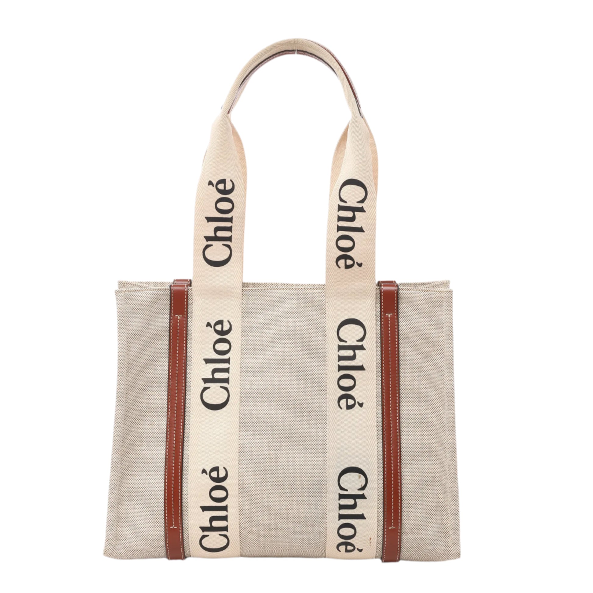 Front view of Chloé Woody Medium Tote Bag in beige canvas with brown leather trim and wide cream-colored logo webbing shoulder straps, displayed against a white background.