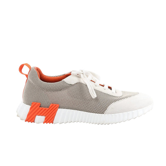 Hermès Bouncing Suede Sneakers in gray, size 44 EU, featuring a mesh and suede upper with white laces, orange interior lining, an orange "H" logo on the midsole, and a ridged white rubber sole, displayed against a white background.