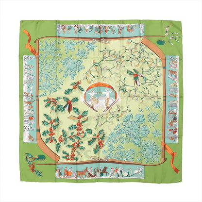 Hermès Carré 90 "Neige d'Antan" Silk Scarf in green, featuring a central design of holly leaves, red berries, mistletoe, and blue snowflakes, bordered with winter-themed illustrations of skiers, sleighs, and festive figures on a green frame.