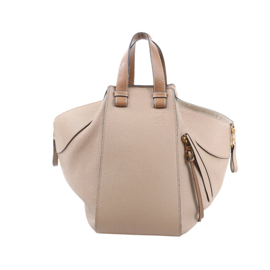 Front view of LOEWE Hammock Medium Leather 2Way Handbag in beige, featuring pebbled leather texture, top handles, adjustable detachable shoulder strap, gold-tone hardware, and expandable side panels against a white background.