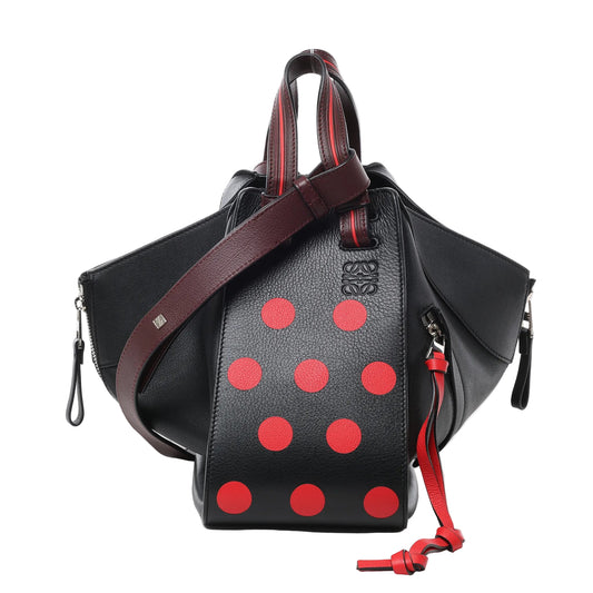 Front view of LOEWE Hammock Small Leather 2Way Handbag in black with red polka dot design, featuring pebbled leather texture, burgundy leather top handles and strap, expandable side panels, and silver-tone hardware against a white background.