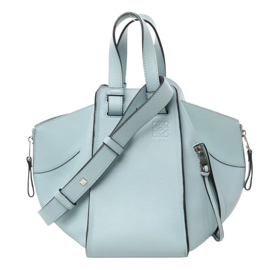 Front view of LOEWE Hammock Small Leather 2Way Handbag in light blue smooth leather with top handles, side zip details, and adjustable shoulder strap, displayed against a white background.