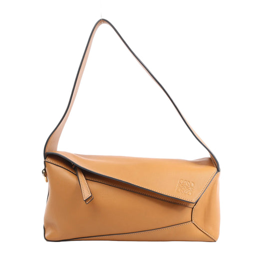 Front view of the LOEWE Puzzle Hobo Shoulder Bag in smooth brown leather, featuring an asymmetric flap closure, geometric panel construction, single shoulder strap, and debossed LOEWE logo, displayed against a white background.