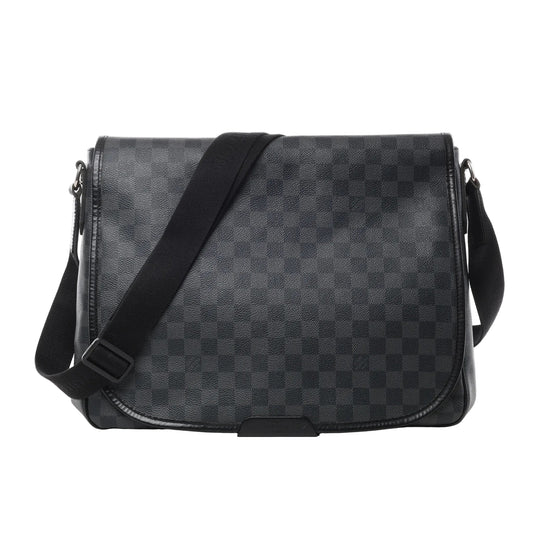 Front view of Louis Vuitton Damier Graphite Daniel MM Shoulder Bag N58029 in black checkered coated canvas, featuring flap closure, adjustable black fabric shoulder strap, and leather trim against a white background.