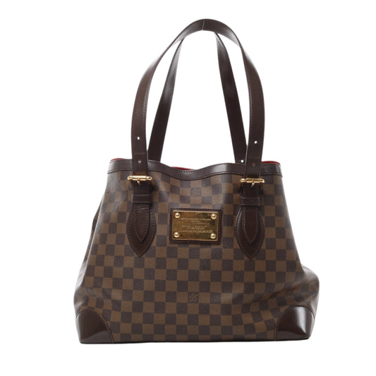 Front view of Louis Vuitton Damier Ebene Hampstead MM handbag N51204, featuring brown checkered coated canvas, dark brown leather trim and handles, gold-tone nameplate, and red interior lining against a white background.