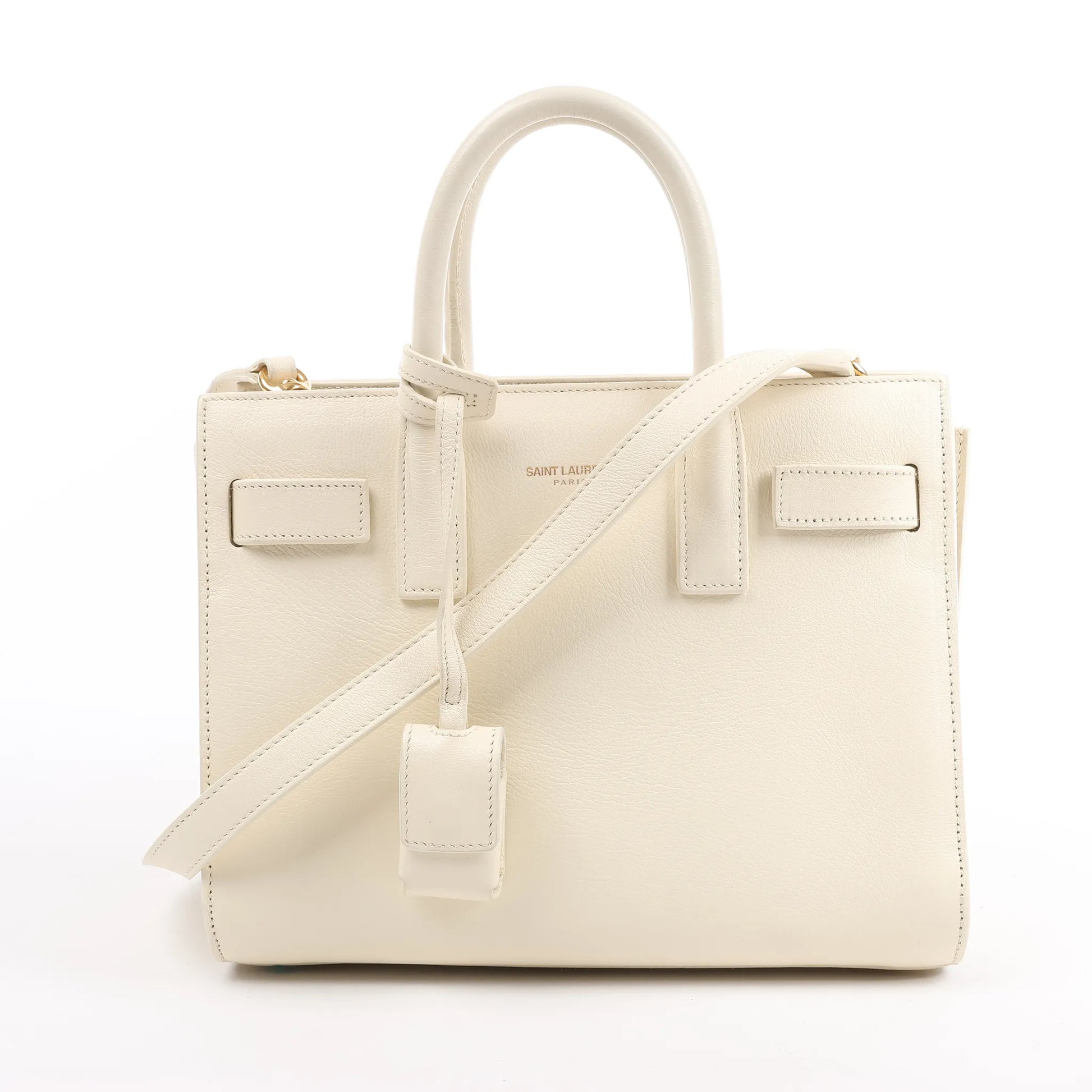 Saint Laurent Paris Sac de Jour Nano handbag in beige grained leather with dual top handles, adjustable and detachable shoulder strap, and signature structured silhouette, displayed against a white background.