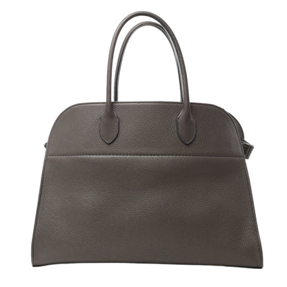 Front view of The Row Soft Margaux 15 Leather Handbag in gray grained leather with dual top handles and a structured, minimalist design, displayed against a white background.